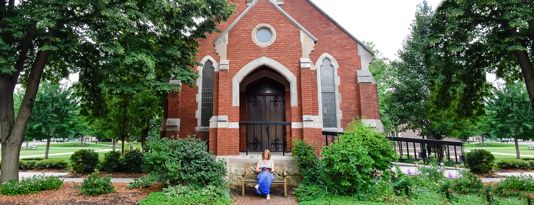 Woman sitting on a bench, reading a book, in front of Alumni Hall at UDTS